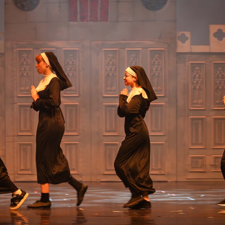 Four female students dressed as nuns walk across the stage during a performance of Sister Act Jr