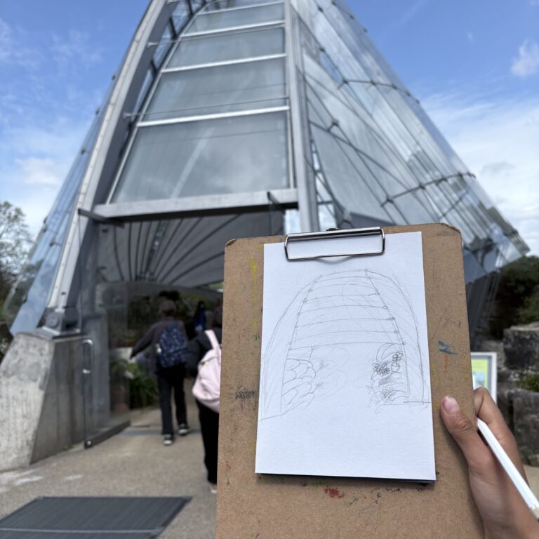 Sketch of a modern glasshouse on a clipboard, held up against the building it was sketched from