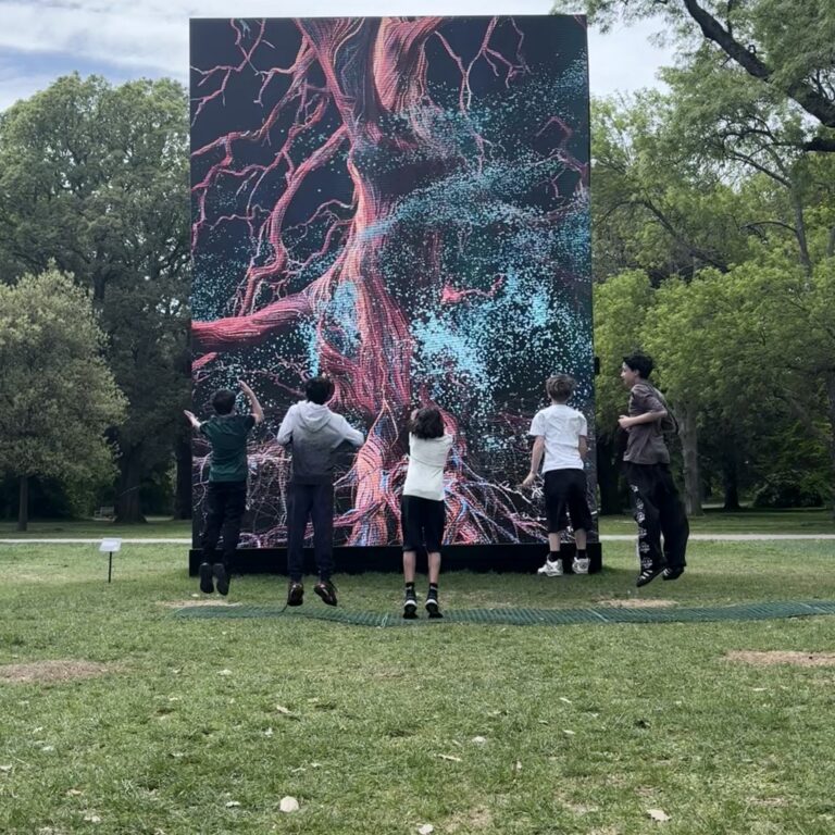 A group of five male students jump in front of a digital art display in the grounds of Kew Gardens