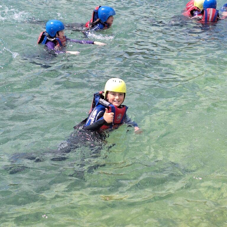 A student wearing a wetsuit gives a thumbs up whilst swimming in a body of water