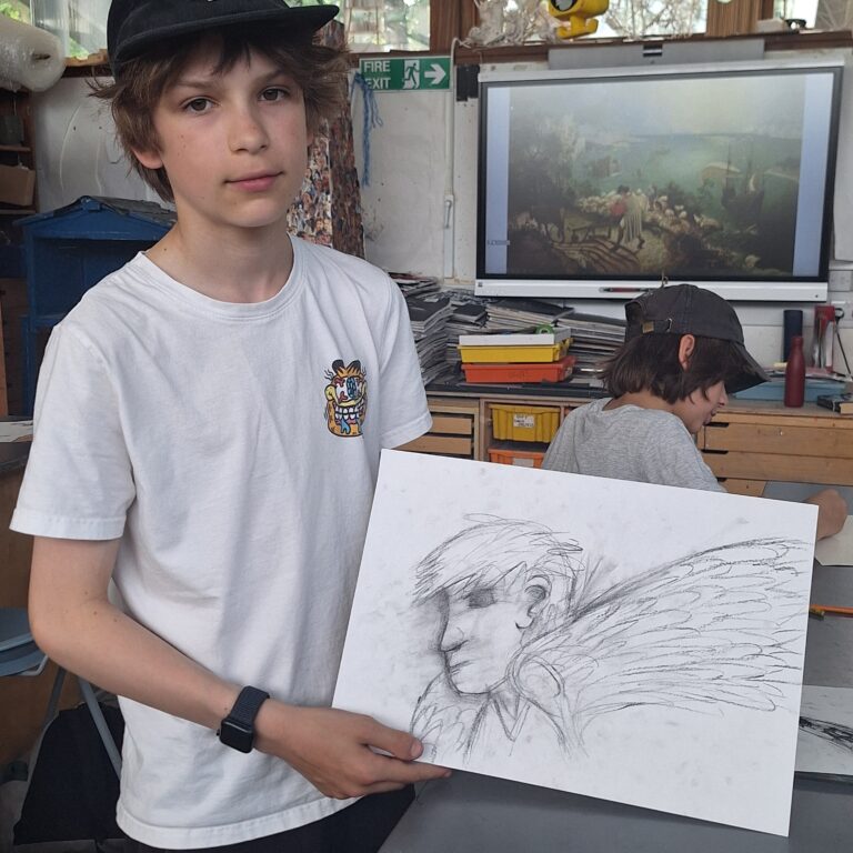 A male student holds his pencil sketch of Icarus in an art room