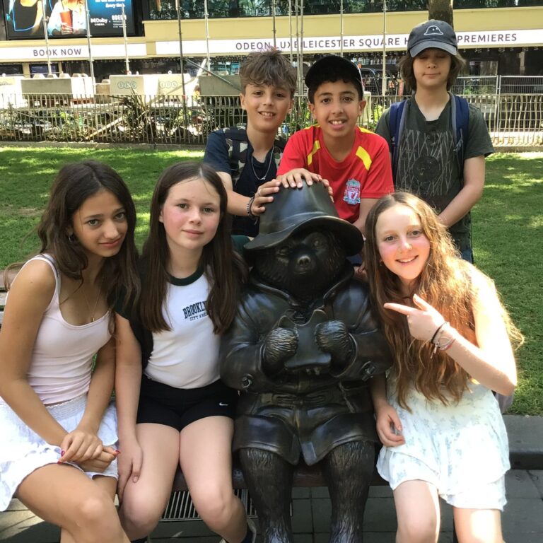 Year 7 students sit around a statue of Paddington Bear in Central London