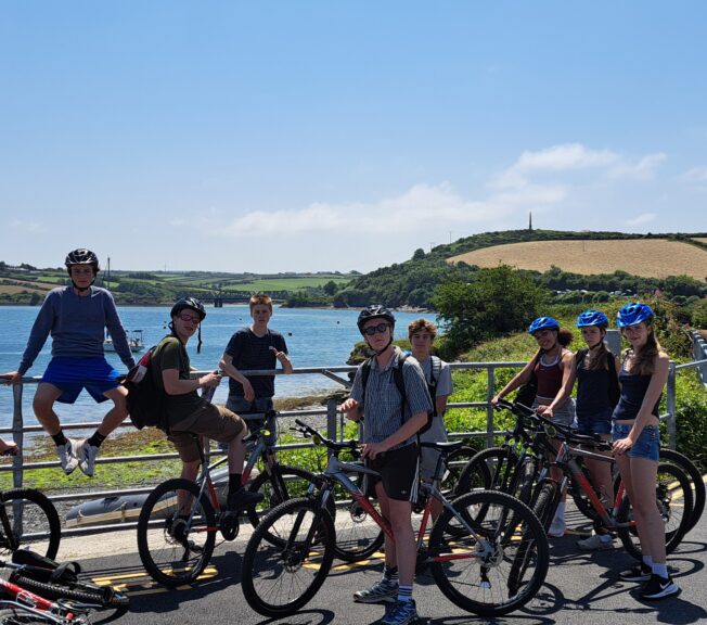 A group of around 10 students pose on bicycles next to a sea view