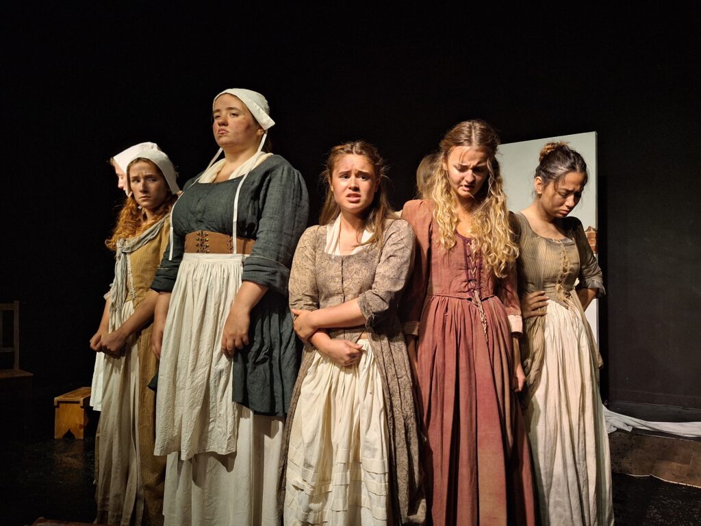 Five female actors in historical dress stand in a close row, looking distressed or defiant, as part of a performance of The Welkin by Performing Arts students at The King Alfred School.