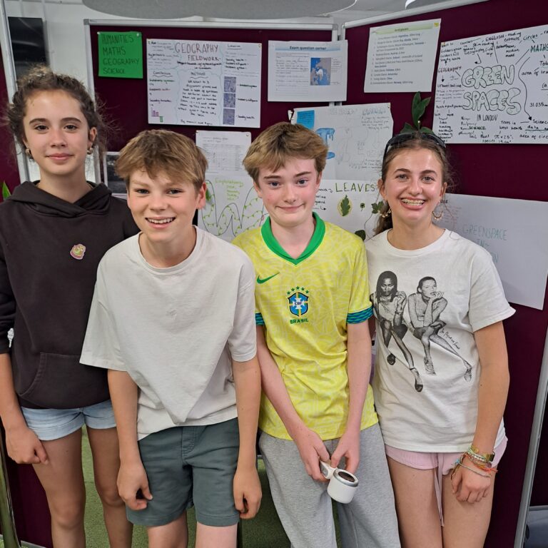 Smiling students - two girls and two boys - stand beside a display of their work charting the biodiversity of Hampstead Heath