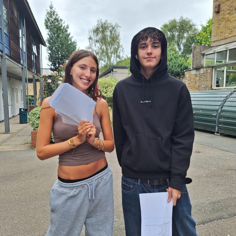 A male and female student smile and hold their GCSE results outside