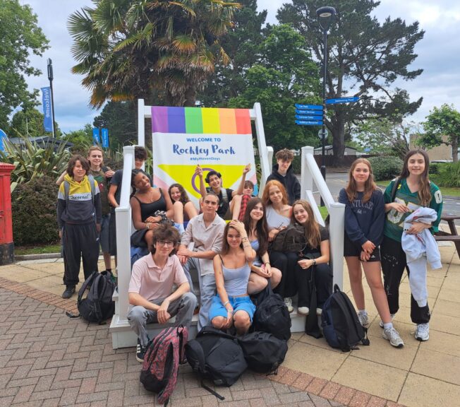 A group or around students pose on and around a giant rainbow-coloured deckchair