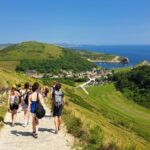 Students are pictured from behind walking down a coastal path, with greenery around them, the sea to the right and a big blue sky
