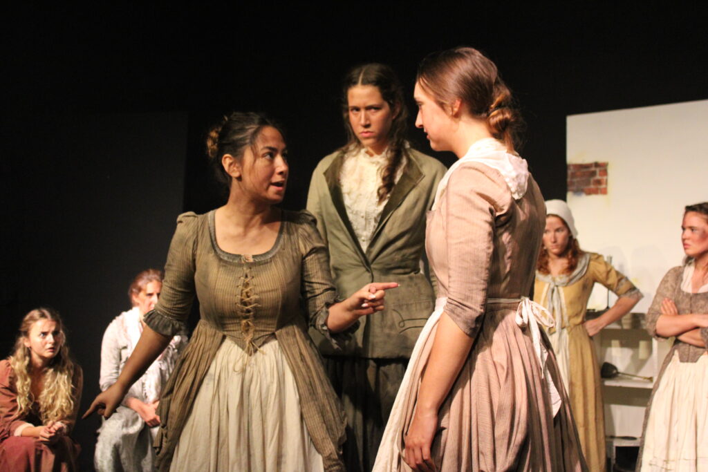 UAL Performing Art students from The King Alfred School wear period costume whilst performing a dramatic scene from The Welkin on stage. One woman points angrily at another whilst another looks on.