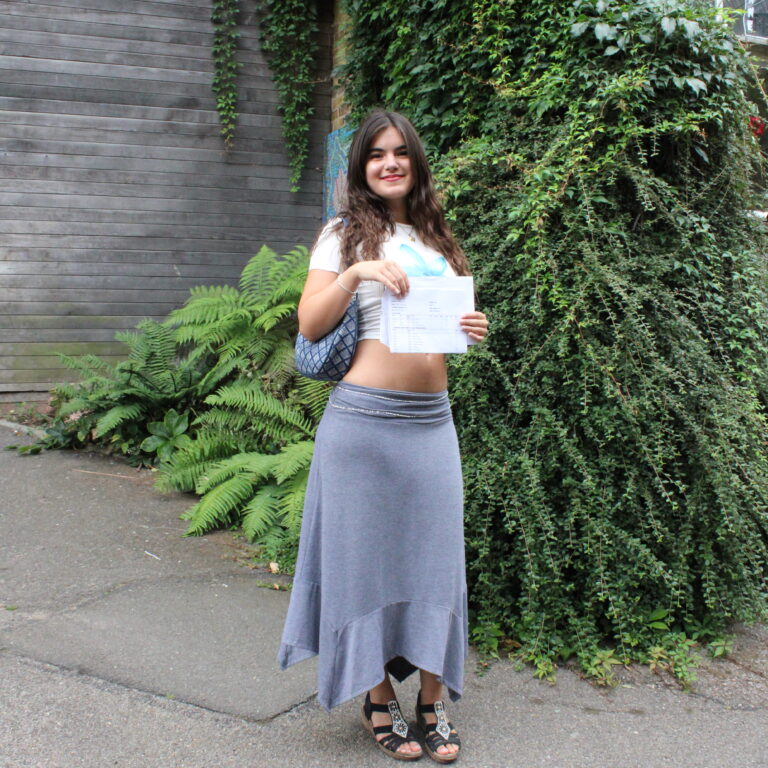 A female student smiles holding her A level exam results outdoors