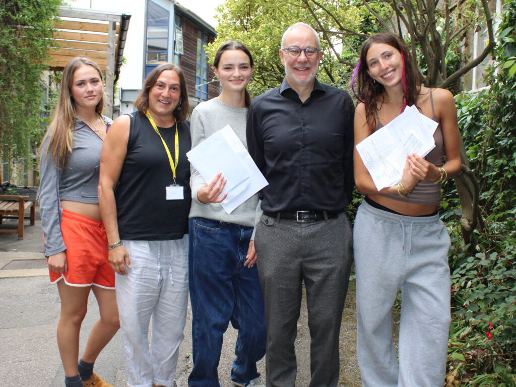 Three female students hold the GCSE exam results alongside a male and female teacher at The King Alfred School