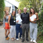Three female students hold the GCSE exam results alongside a male and female teacher at The King Alfred School