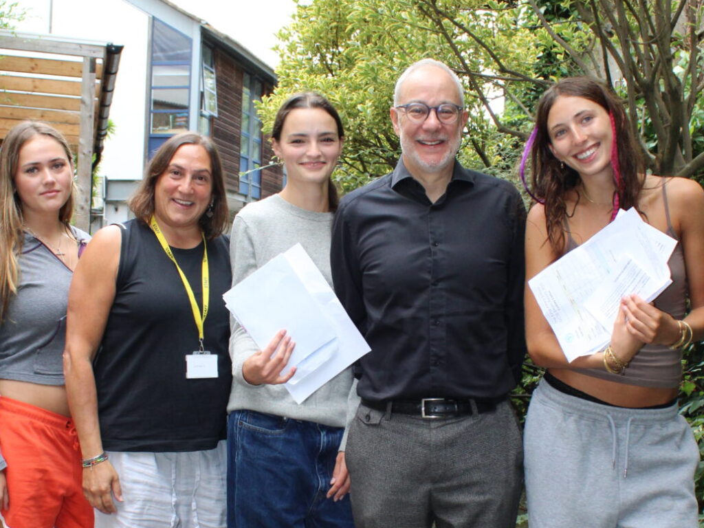 Three female students hold the GCSE exam results alongside a male and female teacher at The King Alfred School