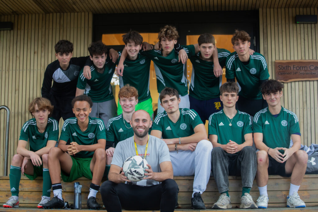 a group of boys dressed in green football shirts sit in two rows with their teacher in the front row holding a football