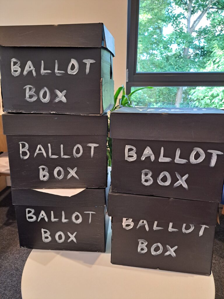 a pile of cardboard boxes painted black with the words 'ballot box' painted on them for use in a mock election at The King Alfred School