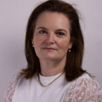 Headshot of a woman with mid length hair wearing a white shirt with beaded shoulders