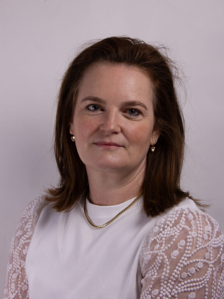 Headshot of a woman with mid length hair wearing a white shirt with beaded shoulders