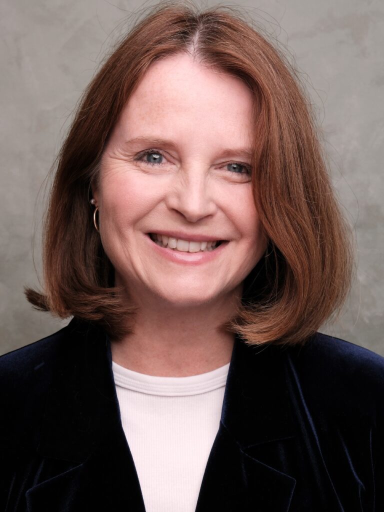 Headshot of a woman with bobbed hair wearing a dark coloured blazer and white tshirt