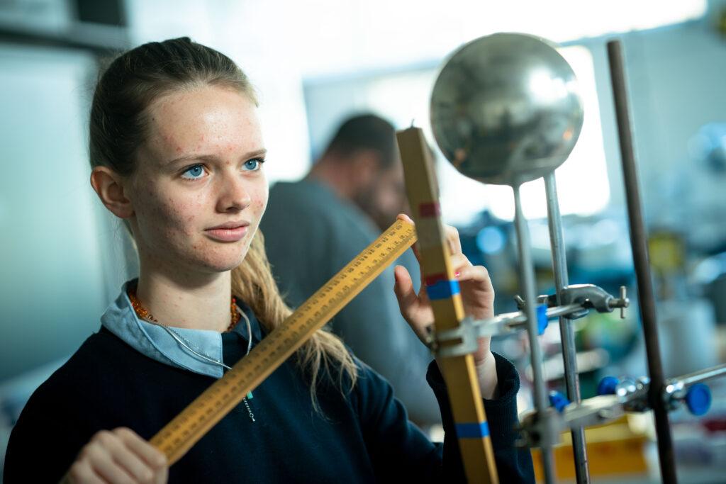 a female student holding a ruler takes measurements in a science classroom