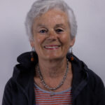 Headshot of a woman with short grey hair wearing a striped tshirt and dark jacket