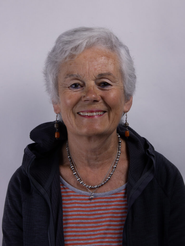 Headshot of a woman with short grey hair wearing a striped tshirt and dark jacket