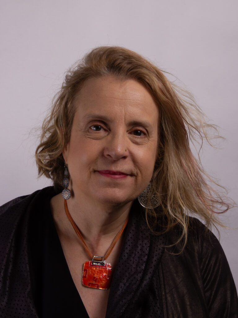 Headshot of a woman with blonde hair wearing a red pendant necklace and dark shirt
