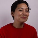 Headshot of a woman with short dark hair wearing a red jumper