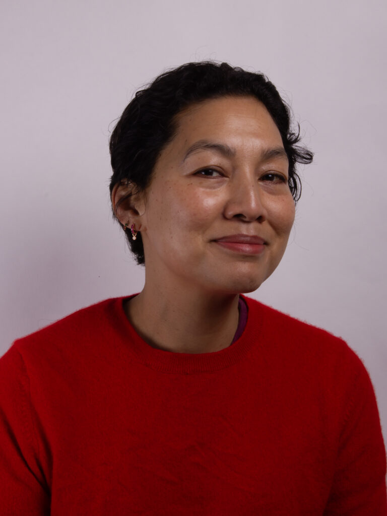 Headshot of a woman with short dark hair wearing a red jumper