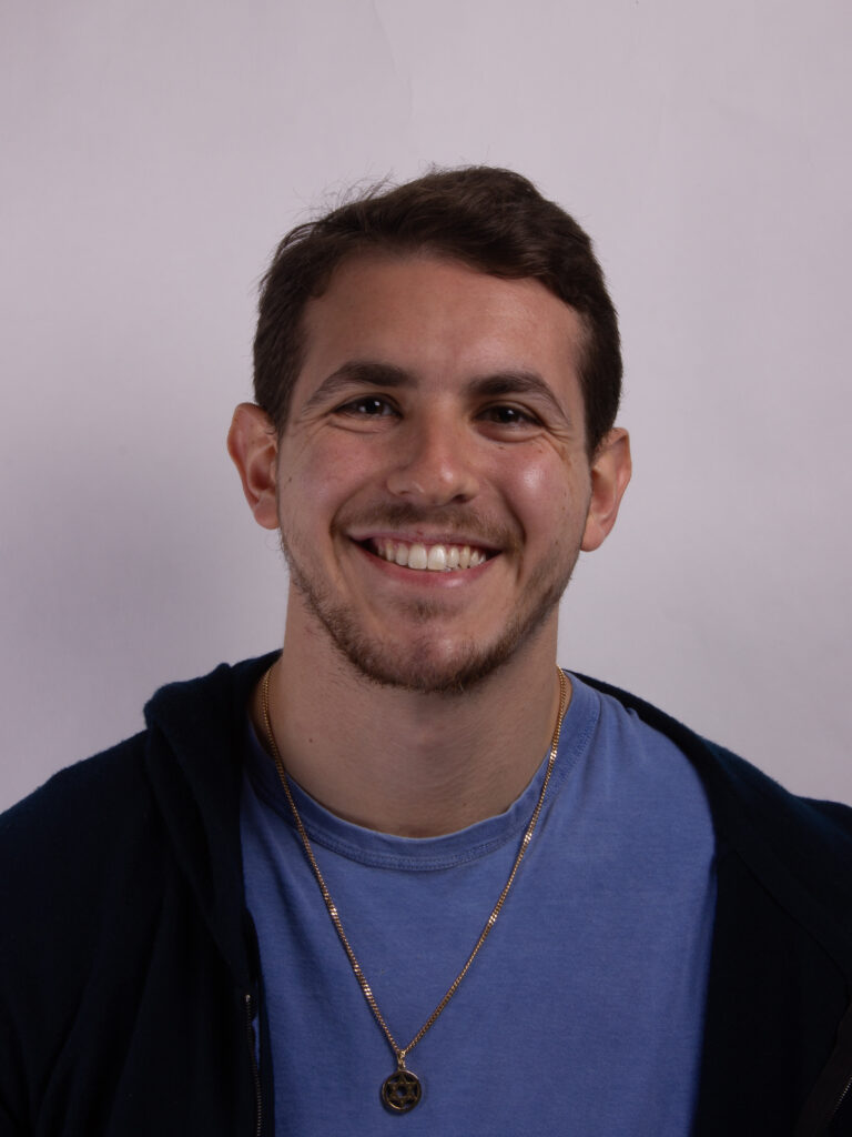 Headshot of a man smiling and wearing a blue tshirt and dark hoodie