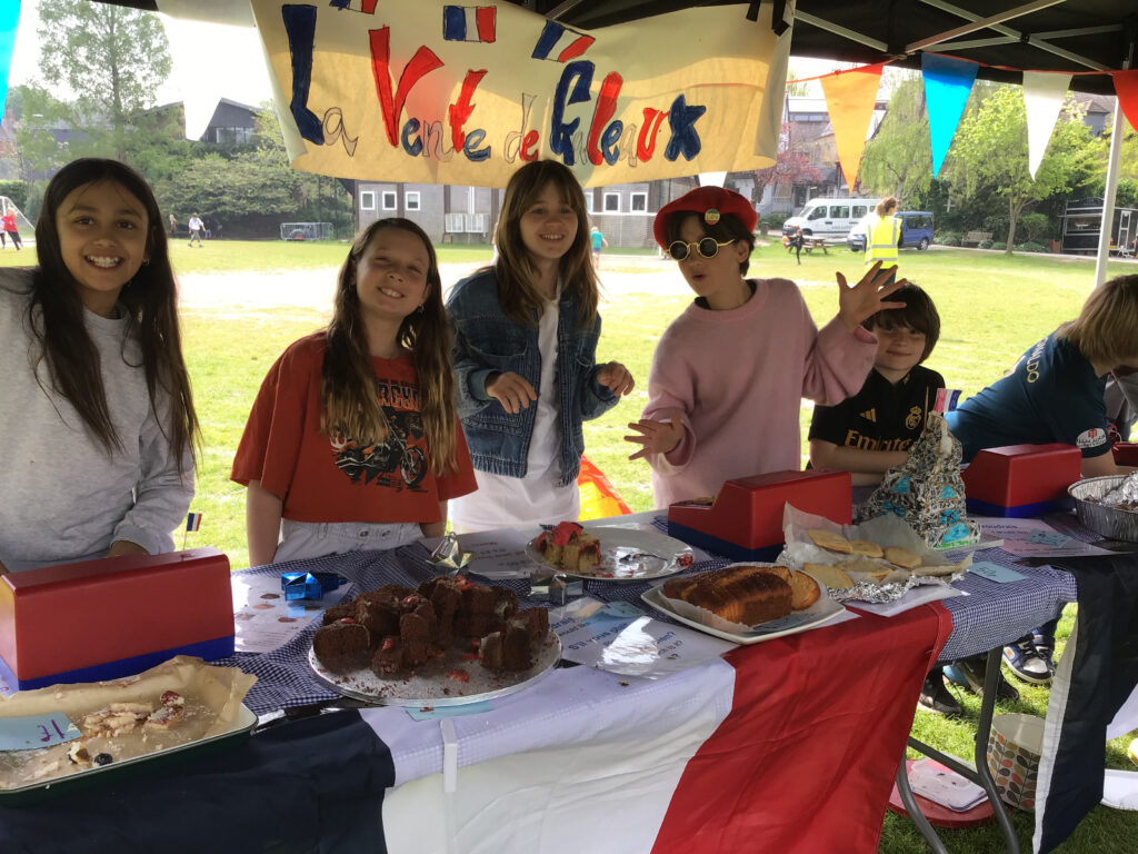students selling cakes at a stall decorated in french signs and the tricolore flag