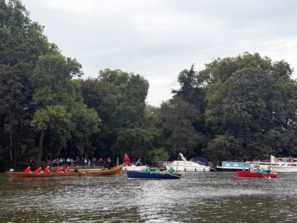 Three wooden row boats on a river, with their crews smiling.