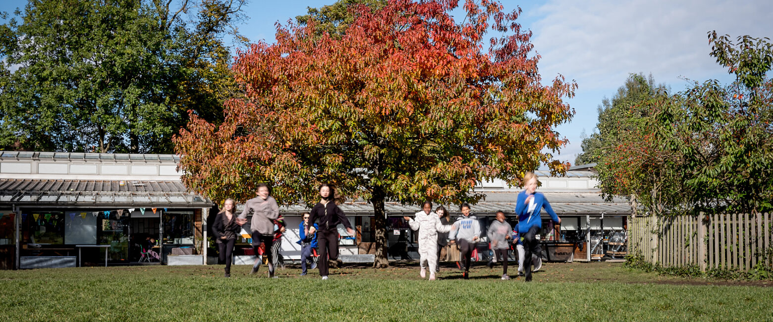 children running across the school field with a autumn tree in the background