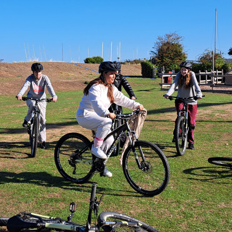 A group of happy students ride bikes on a patch of grass.