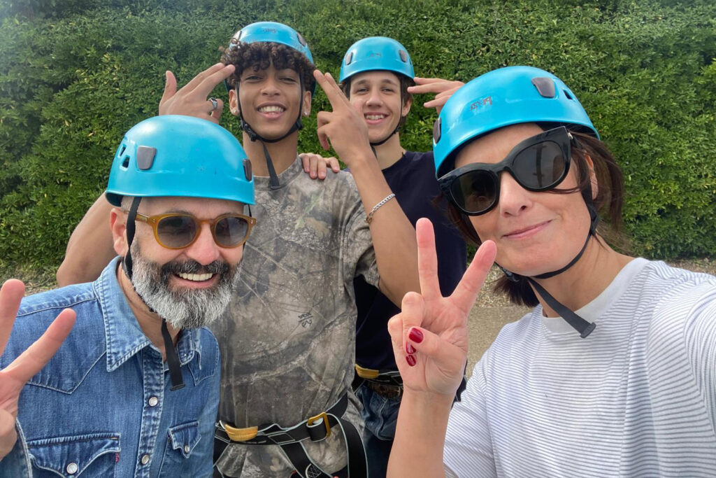 Two Sixth Formers and two teachers wear turquoise helmets, smiling for the camera in front of a green hedge