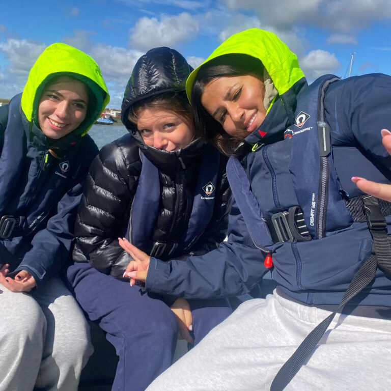 Three Sixth Form students pose for a photograph in a boat on the water, wearing navy life jackets and smiling
