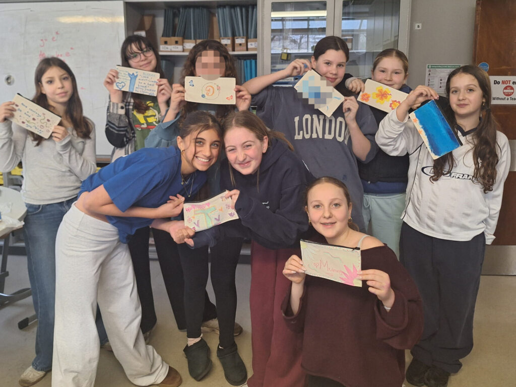 A group of nice female students smile as they pose together in a science lab, holding up pencil cases that they have decorated