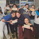 A group of nice female students smile as they pose together in a science lab, holding up pencil cases that they have decorated