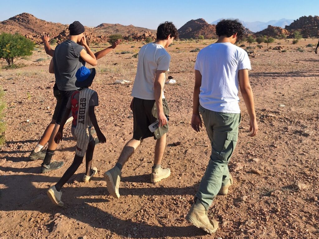 Four older students and smaller boy pictured from behind, walking through the Namibian desert