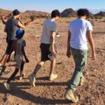 Four older students and smaller boy pictured from behind, walking through the Namibian desert